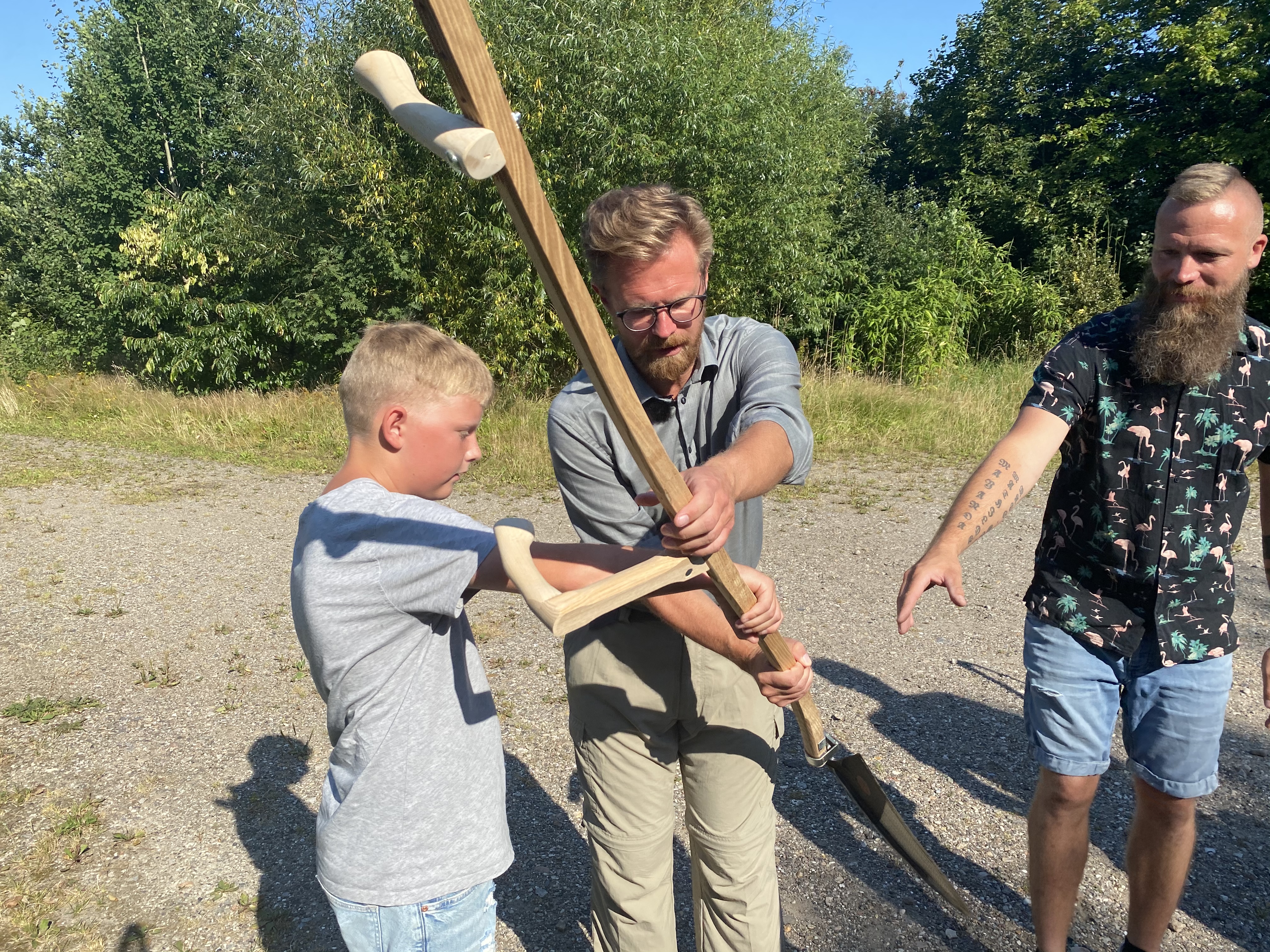 En elev fra Jejsing Friskole viser transportminister Benny Engelbrecht, hvordan man slår græs med en le.